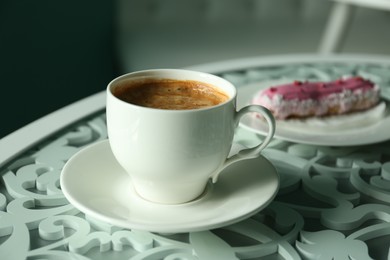 Cup of delicious aromatic coffee and eclair on table indoors