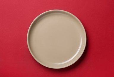 Photo of Empty beige ceramic plate on red background, top view