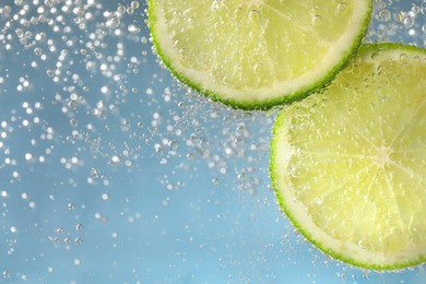 Photo of Juicy lime slices in soda water against light blue background, closeup. Space for text