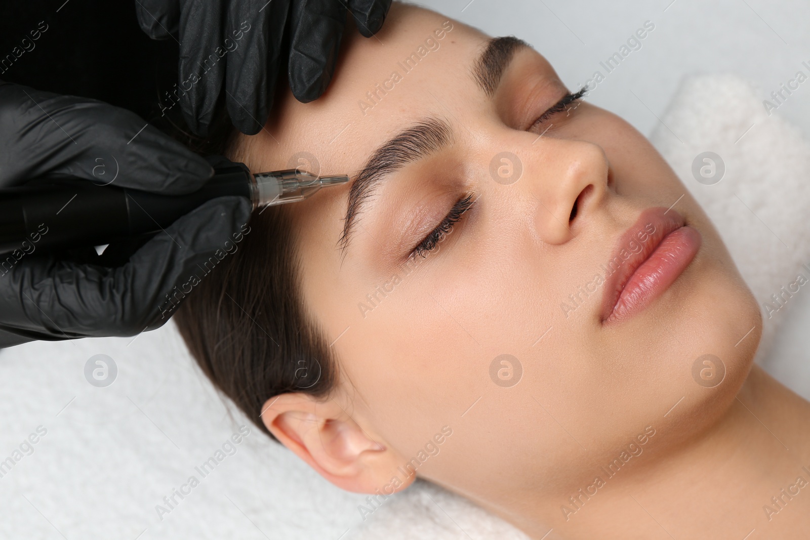 Photo of Beautician making permanent eyebrow makeup to young woman, closeup