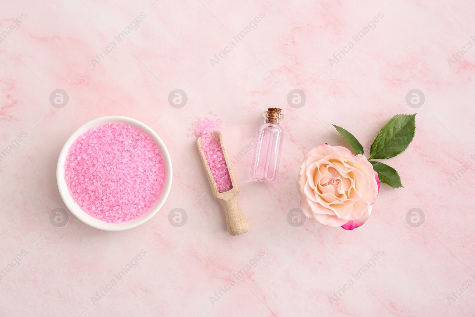 Photo of Bowl and scoop with sea salt, beautiful rose on pink marble table, flat lay