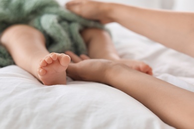 Photo of Mother holding feet of her little baby on bed, closeup