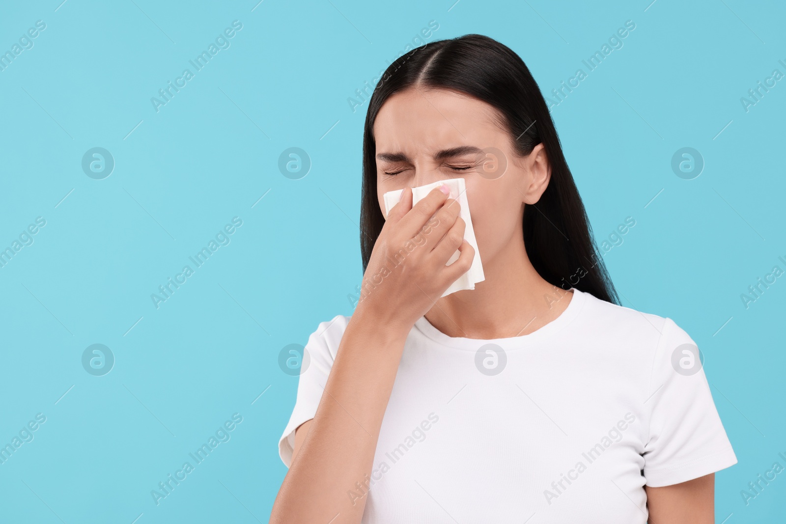 Photo of Suffering from allergy. Young woman blowing her nose in tissue on light blue background. Space for text