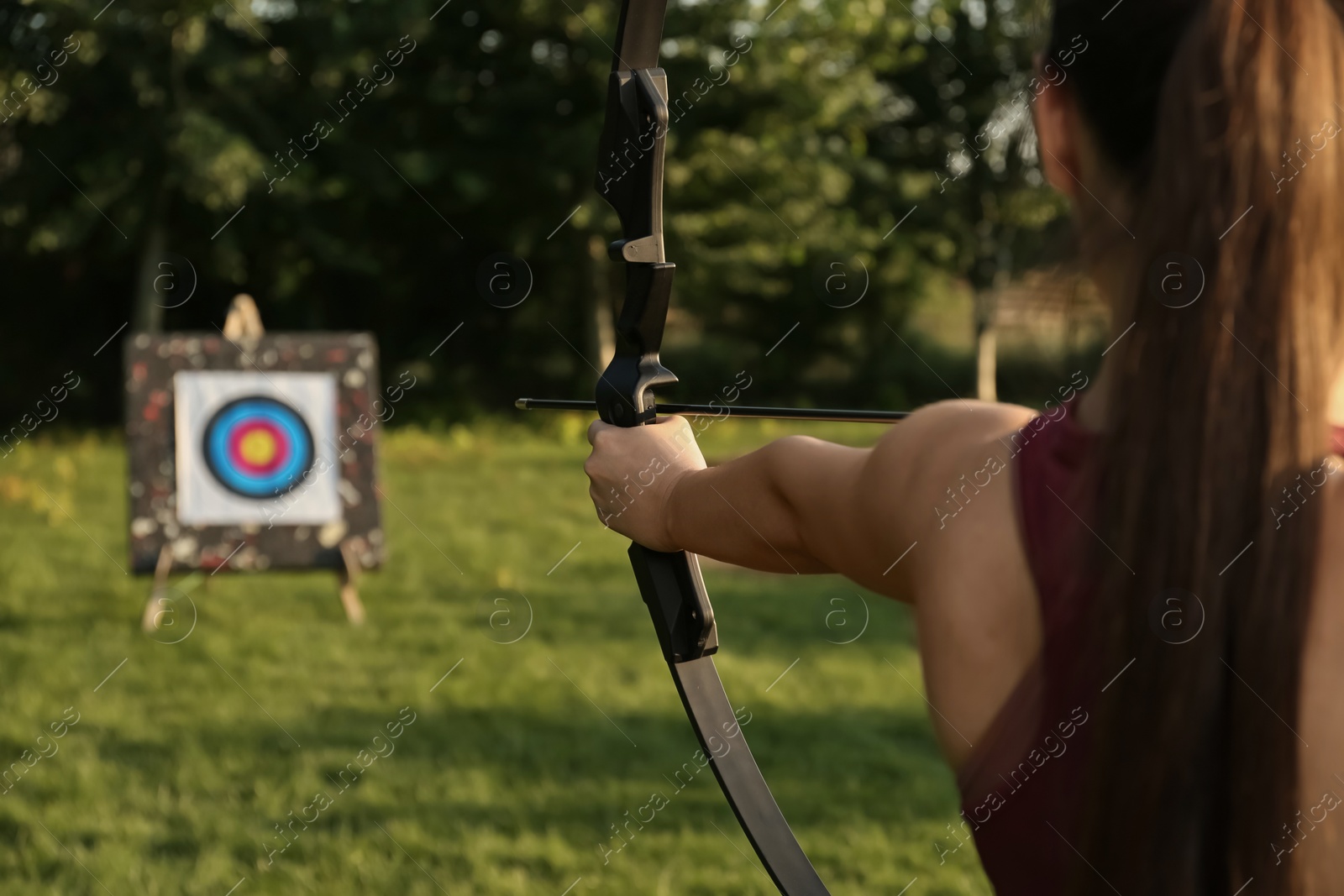 Photo of Woman with bow and arrow aiming at archery target in park, closeup