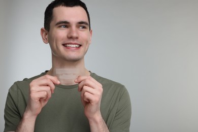 Photo of Young man with whitening strips on light grey background. Space for text