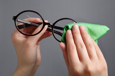 Photo of Woman wiping glasses with microfiber cloth on light grey background, closeup