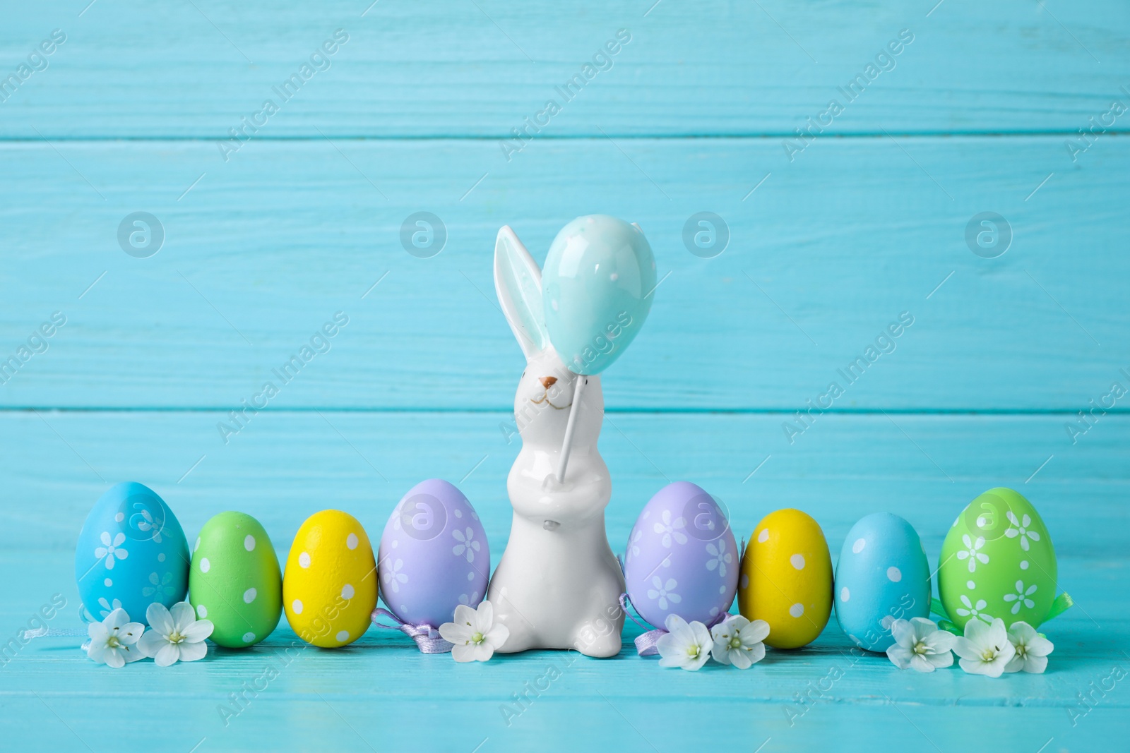 Photo of Easter bunny and painted eggs on light blue wooden background