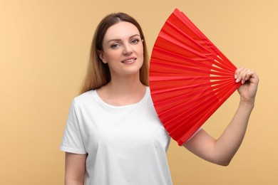 Happy woman with red hand fan on beige background