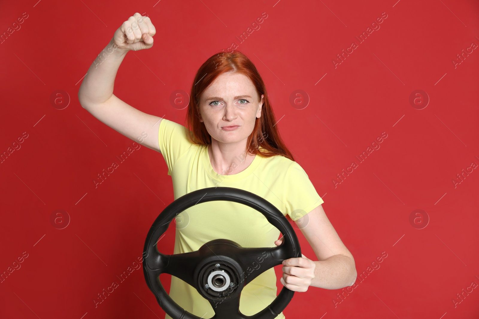 Photo of Emotional young woman with steering wheel on red background