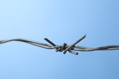 Photo of Metal barbed wire on light blue background, closeup