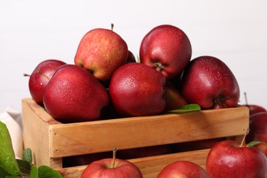 Photo of Fresh red apples with water drops in wooden crate on white background, closeup