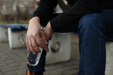 Photo of Addicted man with alcoholic drink on bench outdoors, closeup