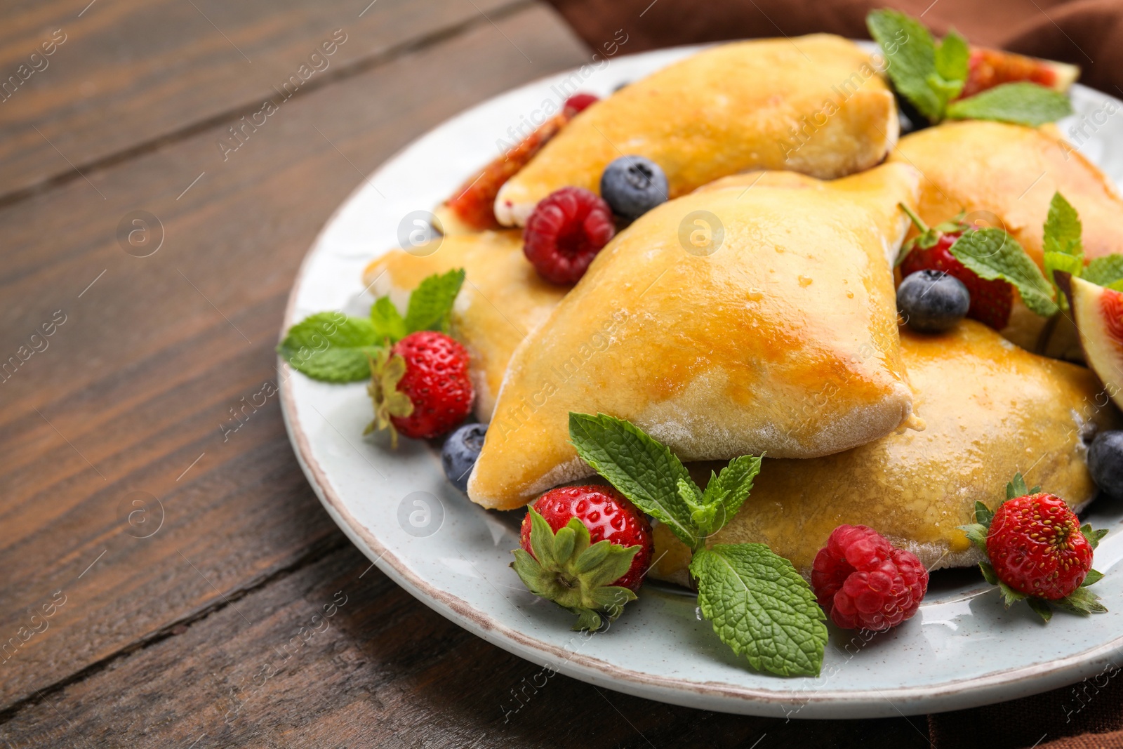Photo of Delicious samosas with berries on wooden table, closeup