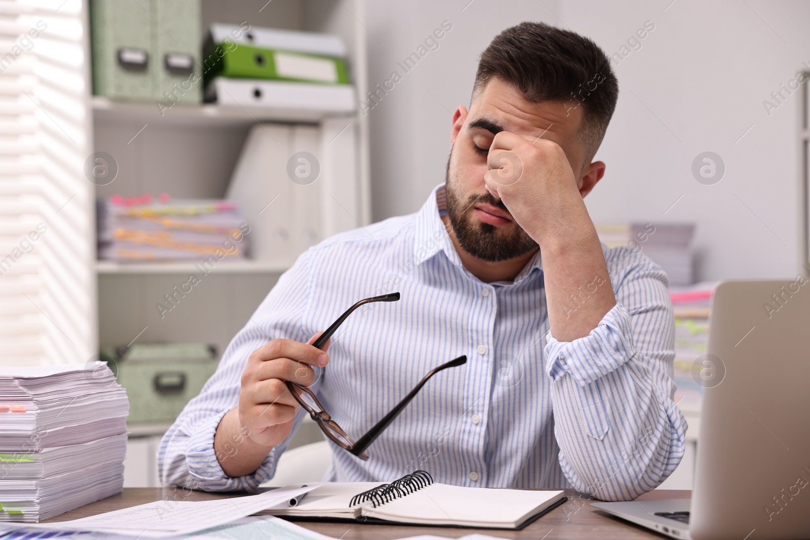 Photo of Overwhelmed man with glasses sitting at table in office