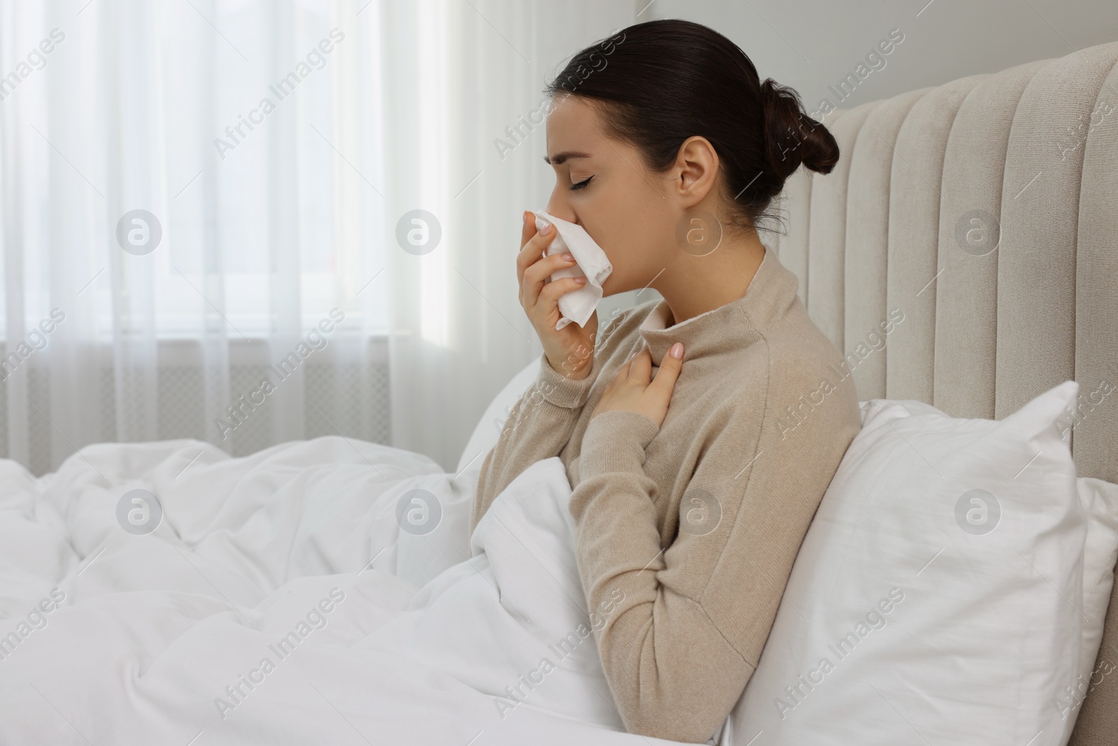 Photo of Sick young woman with tissue in bed at home, space for text