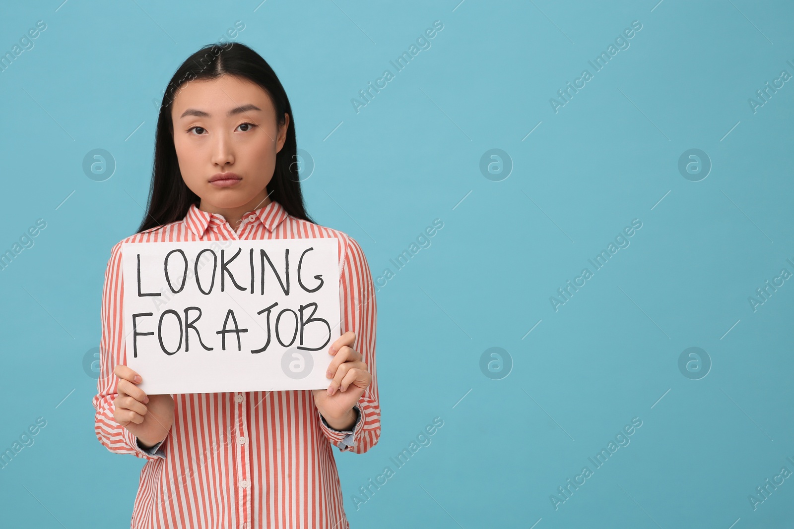 Photo of Unemployed Asian woman holding sign with phrase Looking For A Job on light blue background. Space for text