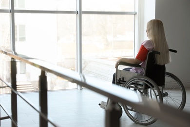 Photo of Mature woman sitting in wheelchair near window at home