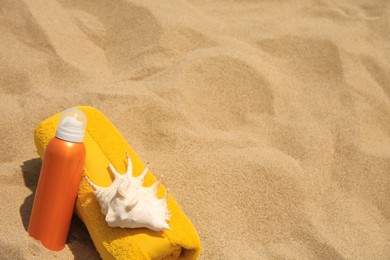 Photo of Sunscreen, seashell and rolled towel on sandy beach, space for text. Sun protection