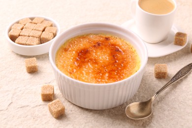 Photo of Delicious creme brulee in bowl, sugar cubes, coffee and spoon on light textured table, closeup