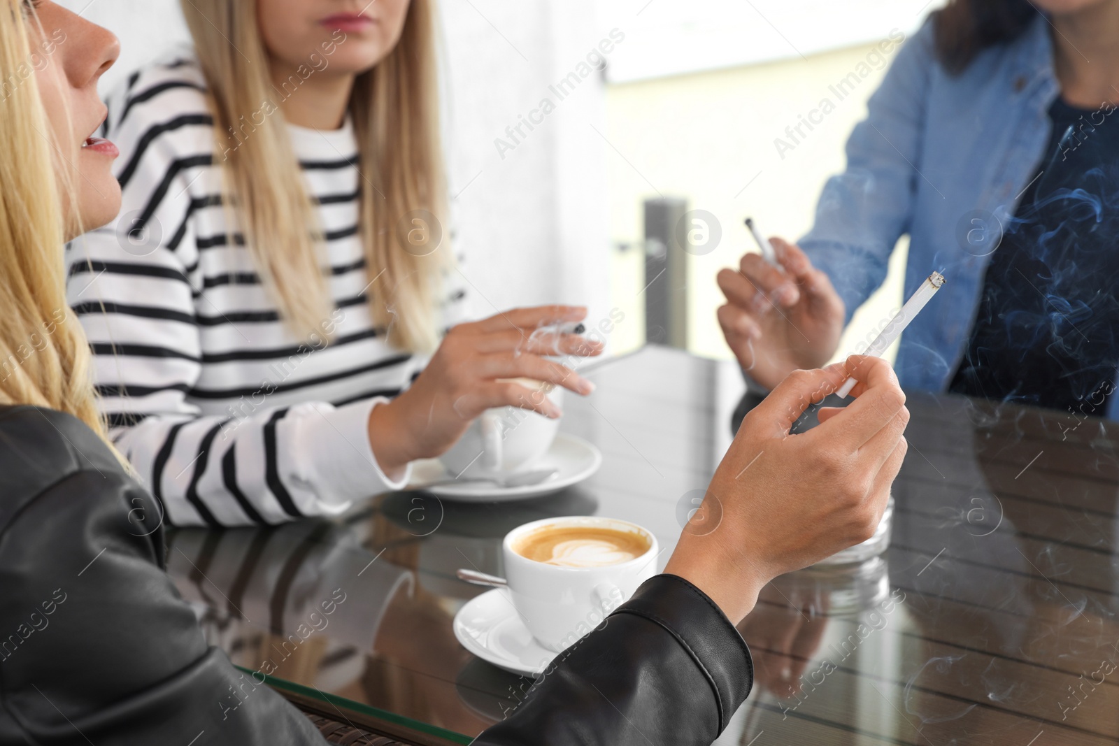 Photo of Women smoking cigarettes at table in outdoor cafe