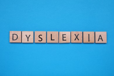 Photo of Wooden cubes with word Dyslexia on light blue background, flat lay