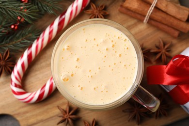 Glass of delicious eggnog, candy cane and anise stars on wooden table, flat lay