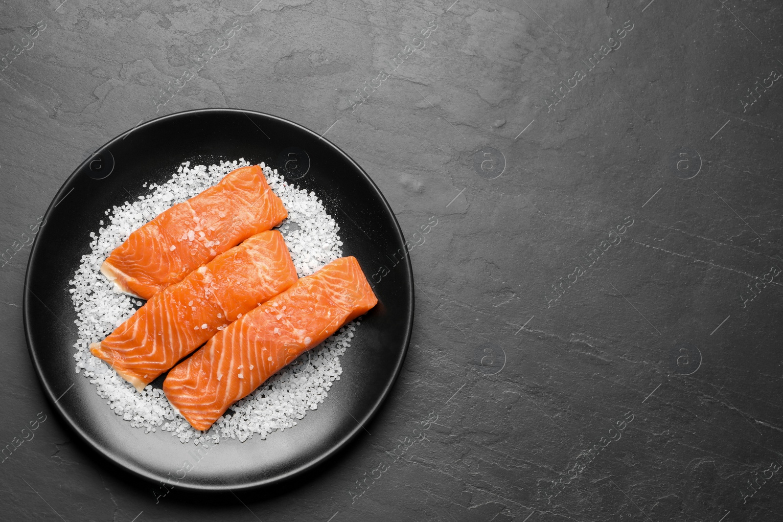Photo of Fresh raw salmon with salt on black table, top view. Space for text