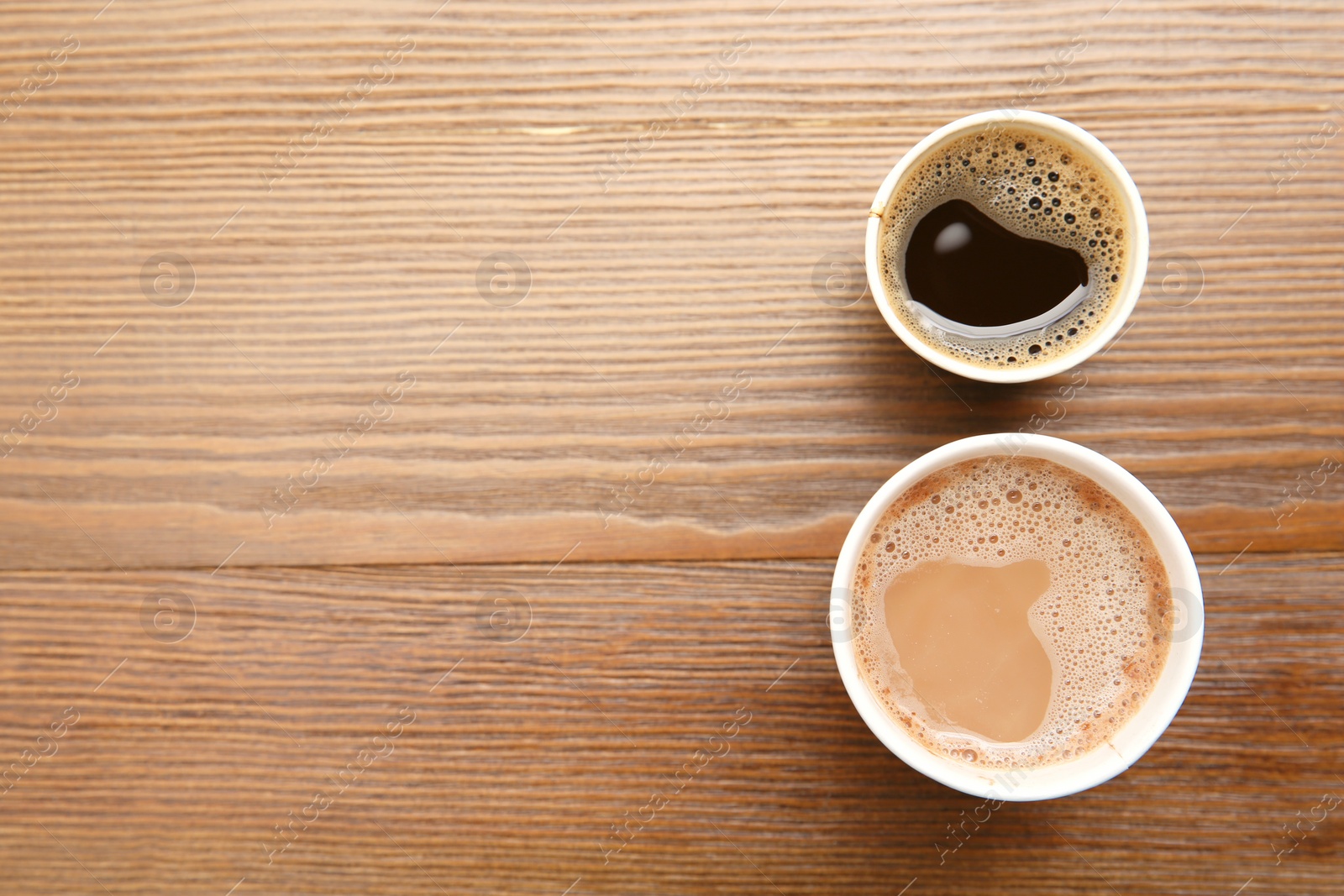 Photo of Cardboard cups of coffee on wooden table, top view. Space for text