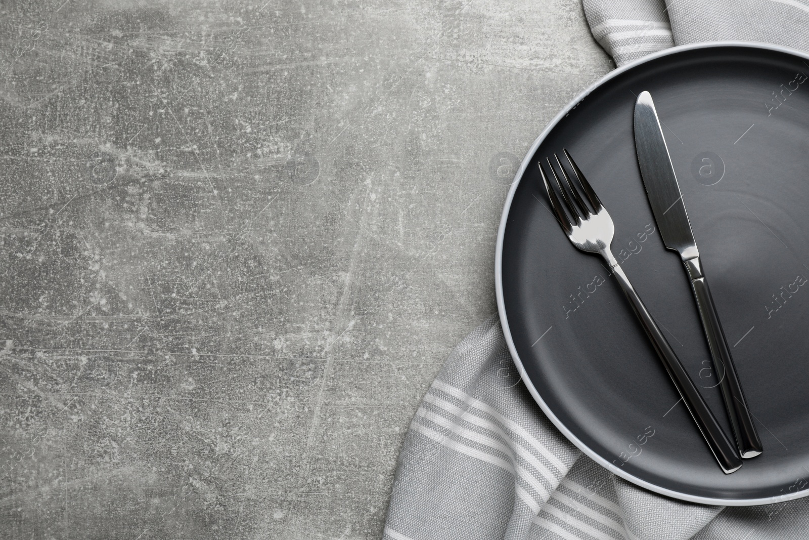 Photo of New dark plate with cutlery and napkin on light grey table, top view. Space for text