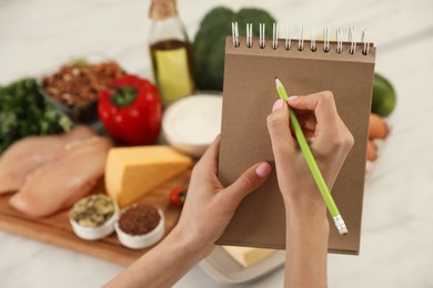 Woman writing in notebook near products at table, closeup. Keto diet