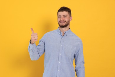 Photo of Young man showing thumb up on orange background