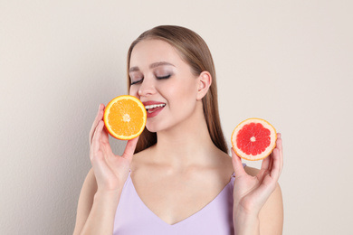 Young woman with cut orange and grapefruit on beige background. Vitamin rich food