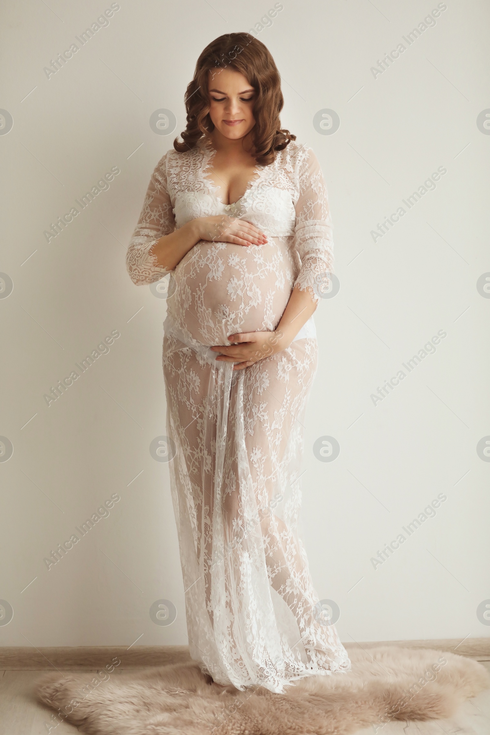 Photo of Young pregnant woman in elegant dress near light wall indoors