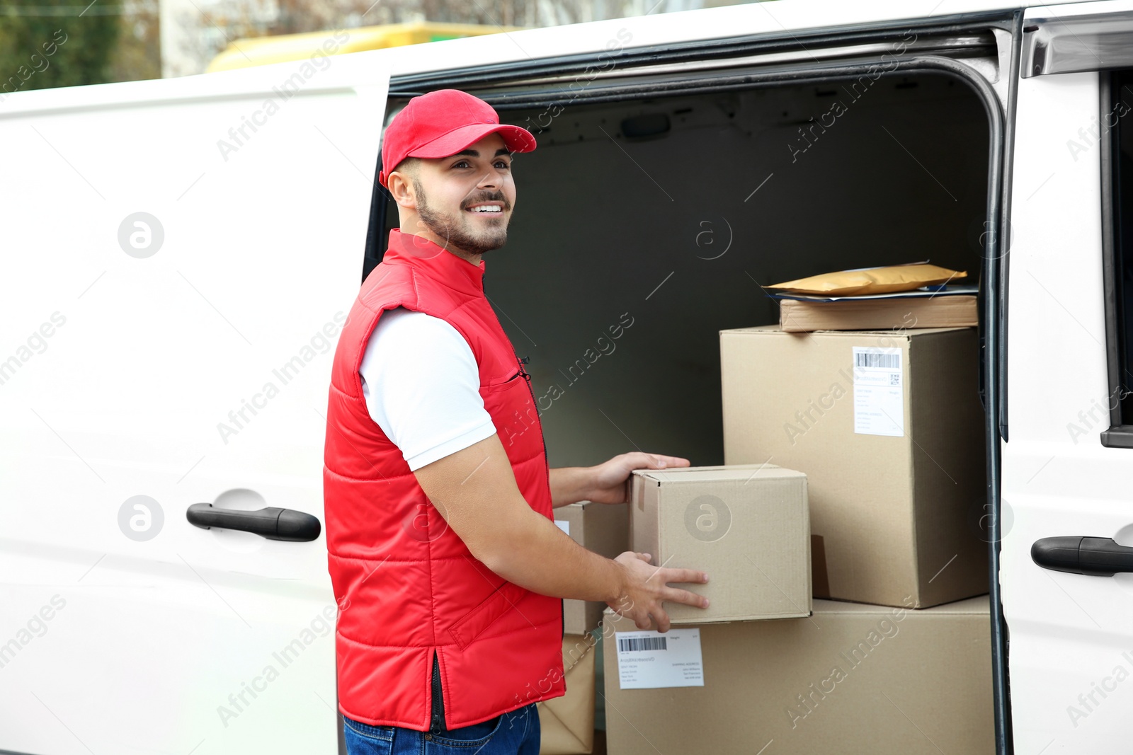 Photo of Young courier near van with parcels outdoors