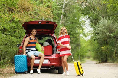 Happy couple near car trunk with suitcases outdoors. Space for text