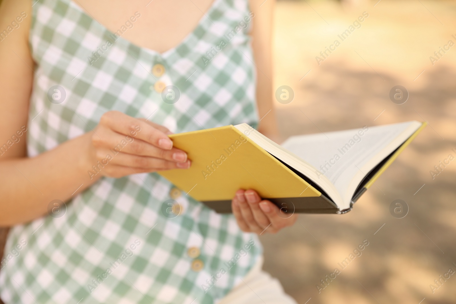 Photo of Young woman reading book outdoors, closeup view