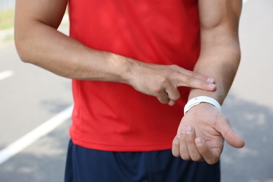 Photo of Young man checking pulse after training outdoors, closeup
