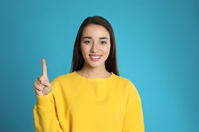 Photo of Woman showing number one with her hand on light blue background