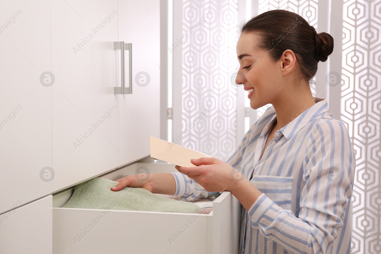 Photo of Woman putting scented sachet into drawer with towels indoors