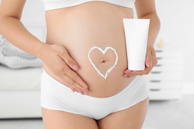 Heart painted with body cream on pregnant woman's belly at home, closeup