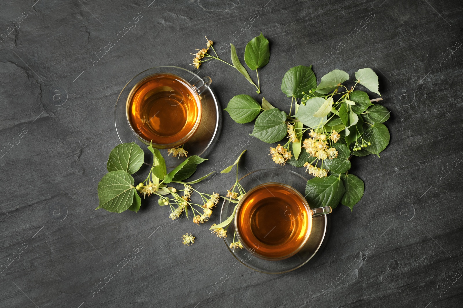 Photo of Flat lay composition with tasty tea and linden blossom on black table