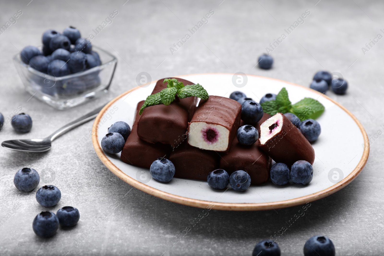 Photo of Delicious glazed curd snacks with fresh blueberries and mint on light grey table