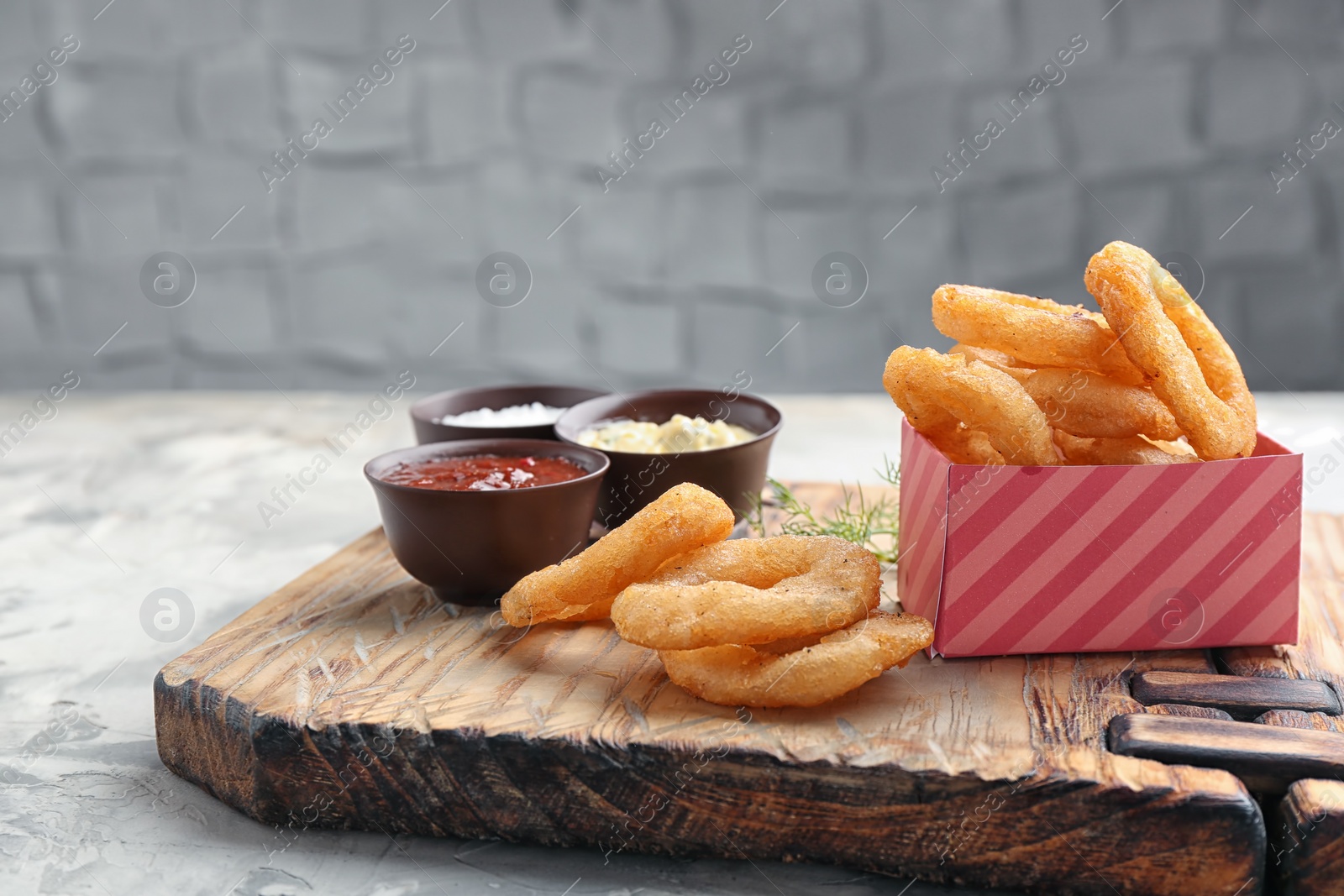 Photo of Fried onion rings served with sauces on wooden board