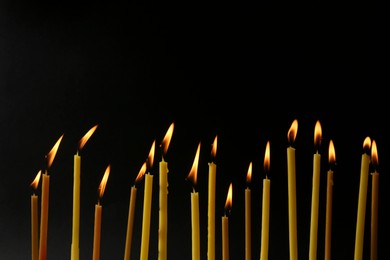 Many burning church candles on black background