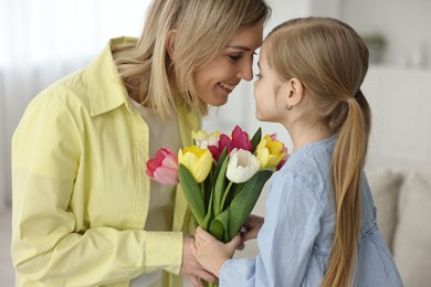 Photo of Little daughter congratulating her mom with bouquet of tulips at home. Happy Mother's Day