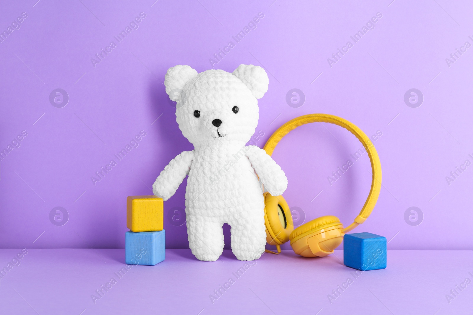 Photo of Baby songs. Toy bear, headphones and cubes on violet background