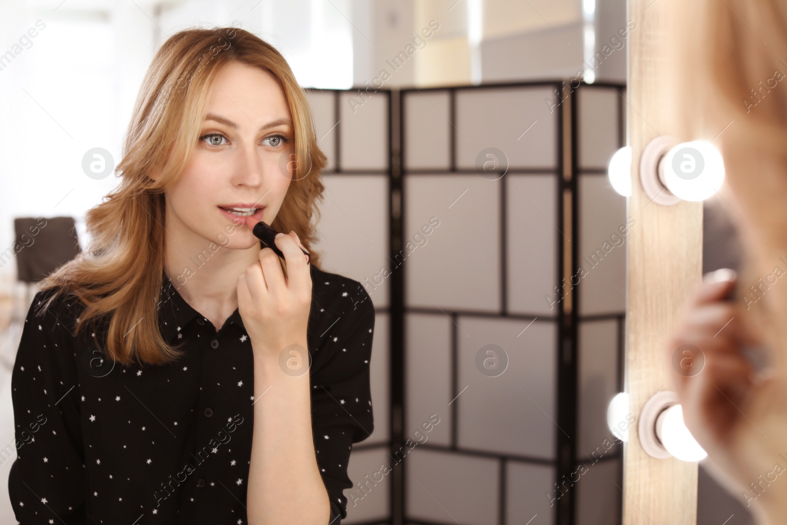 Photo of Young woman applying makeup near mirror in dressing room