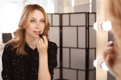 Young woman applying makeup near mirror in dressing room