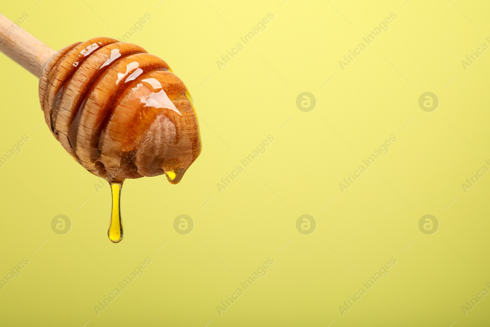 Photo of Delicious honey flowing down from dipper against yellow background, closeup. Space for text