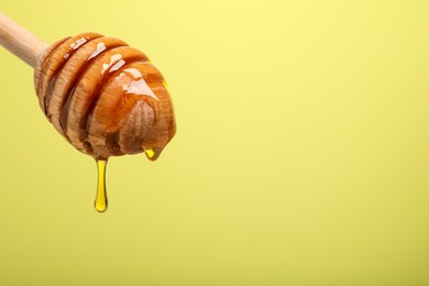 Delicious honey flowing down from dipper against yellow background, closeup. Space for text